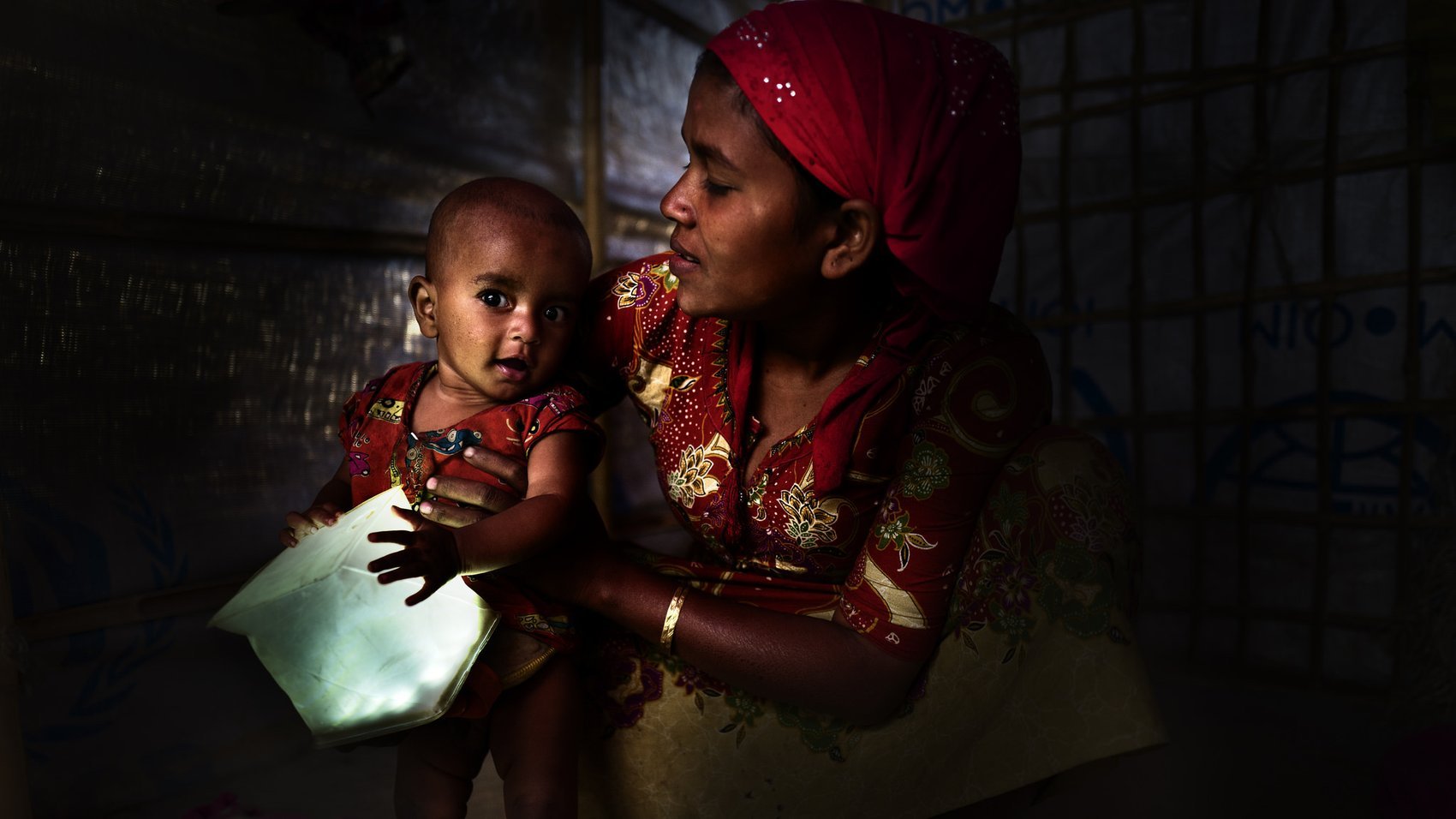 Woman holds her child who is playing with the a LuminAID solar lantern.
